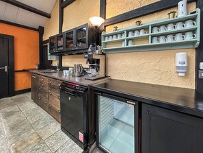 Une cuisine équipée d’une machine à café, d’un lave-vaisselle et d’une étagère où sont rangées des tasses.