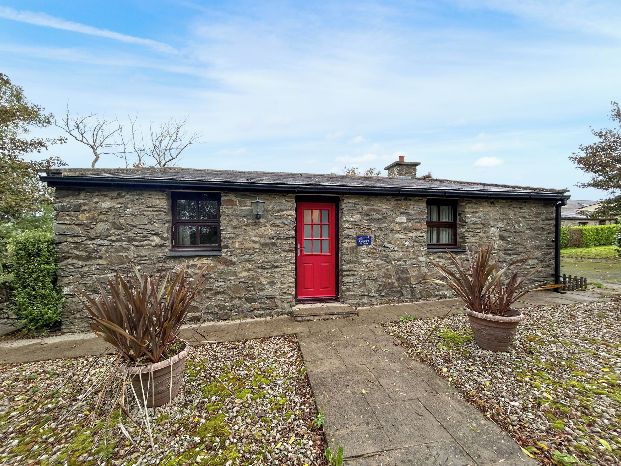 Une petite maison en pierre avec une porte rouge, une petite fenêtre et une enseigne indiquant qu’il s’agit d’un lieu proposant des chambres et le petit-déjeuner.