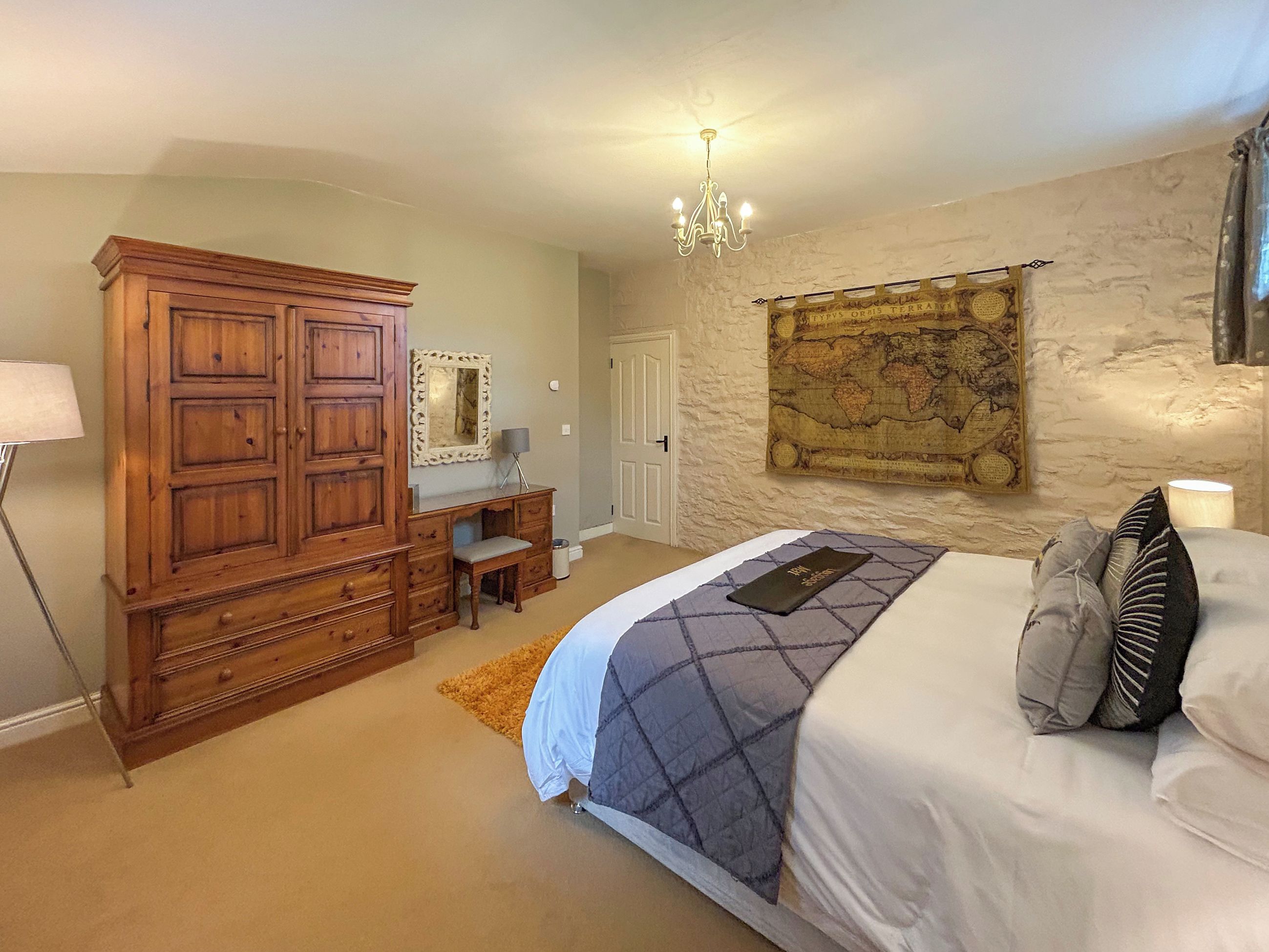 Une chambre à coucher avec un lit, une commode, un bureau, une chaise, une carte accrochée au mur et un lustre.