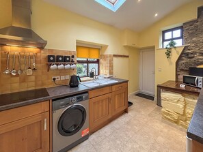 Une cuisine moderne dotée d’un lave-linge encastré, d’un four à micro-ondes et d’un mur décoratif en pierre.