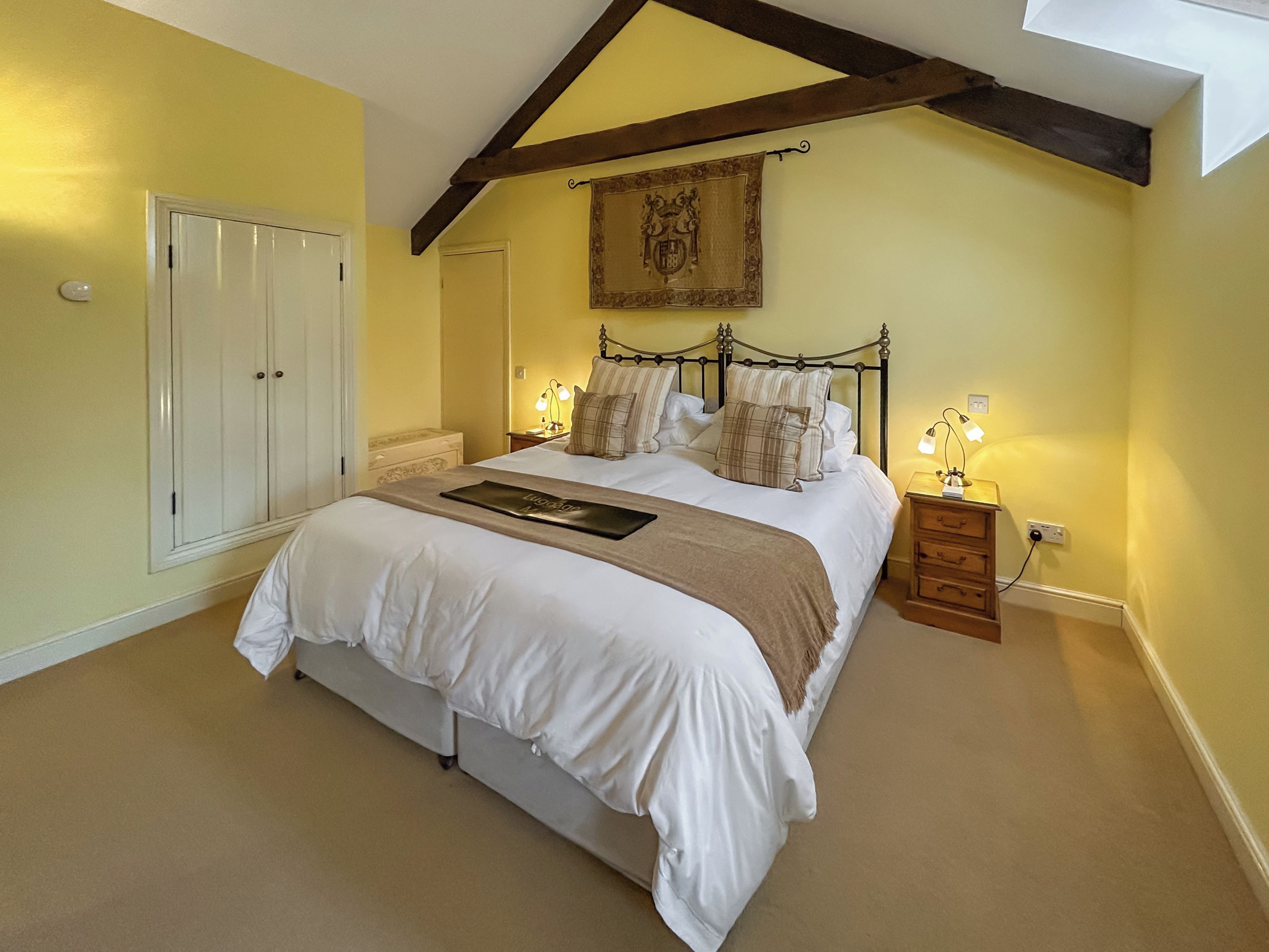A bedroom with a large bed, a wardrobe, a nightstand with a lamp, and a decorative wall hanging.