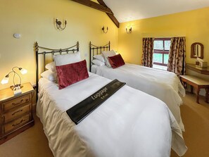 Ein Hotelzimmer mit zwei Betten, einem Holznachtkästchen, einem Schreibtisch und einem Fenster mit Vorhängen.