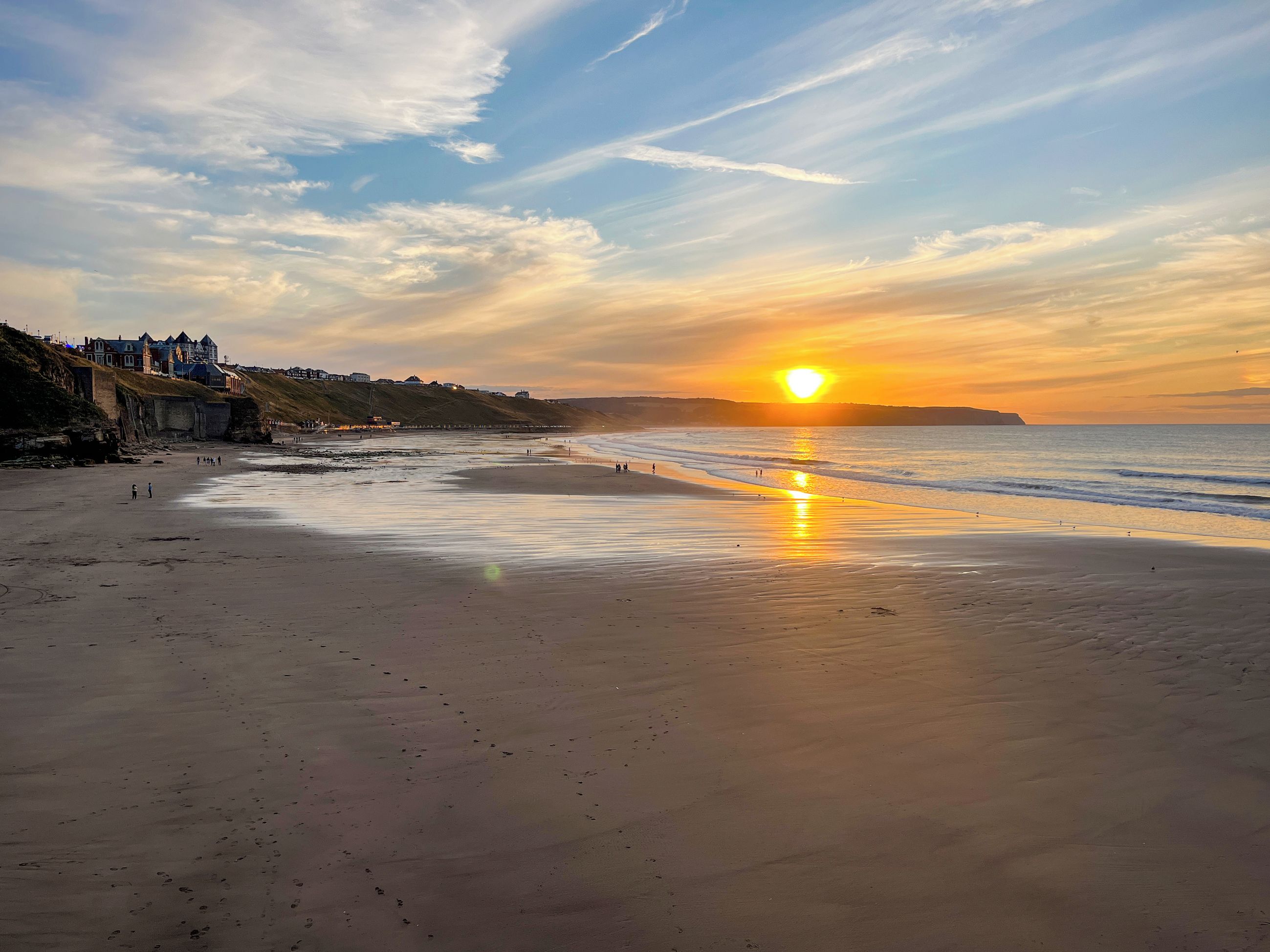 A beach with a sunset, a sandy shore, and buildings in the background.