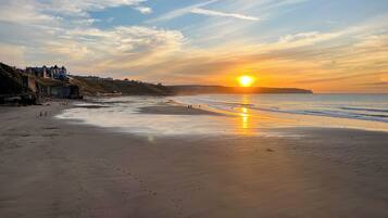 A beach with a sunset, a sandy shore, and buildings in the background.