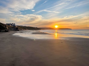 Een strand bij zonsondergang, met een zandstrand en gebouwen op de achtergrond.
