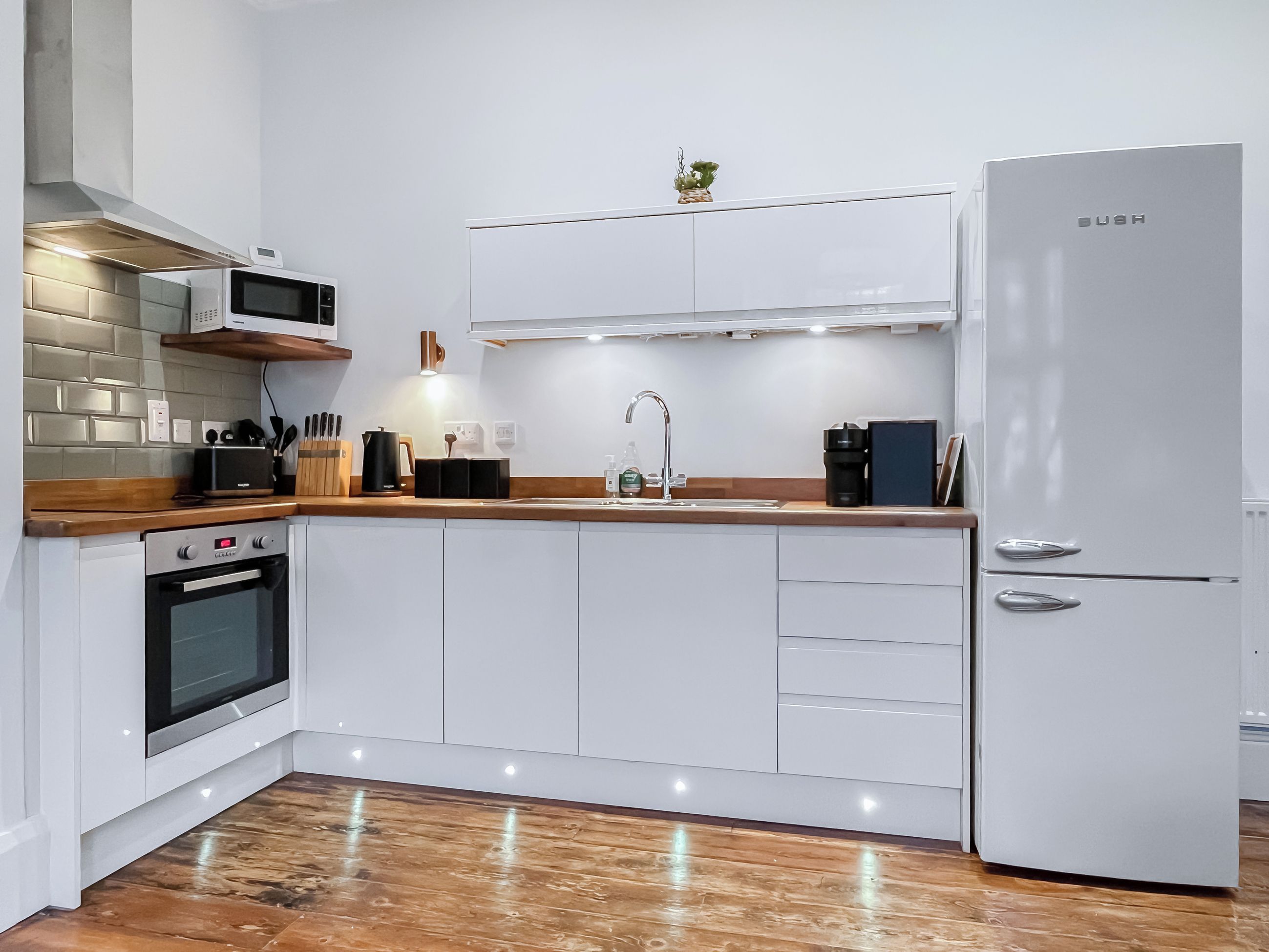A modern kitchen with white cabinetry, a built-in oven, a microwave, a sink, and a refrigerator.