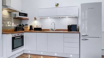 A modern kitchen with white cabinetry, a built-in oven, a microwave, a sink, and a refrigerator.