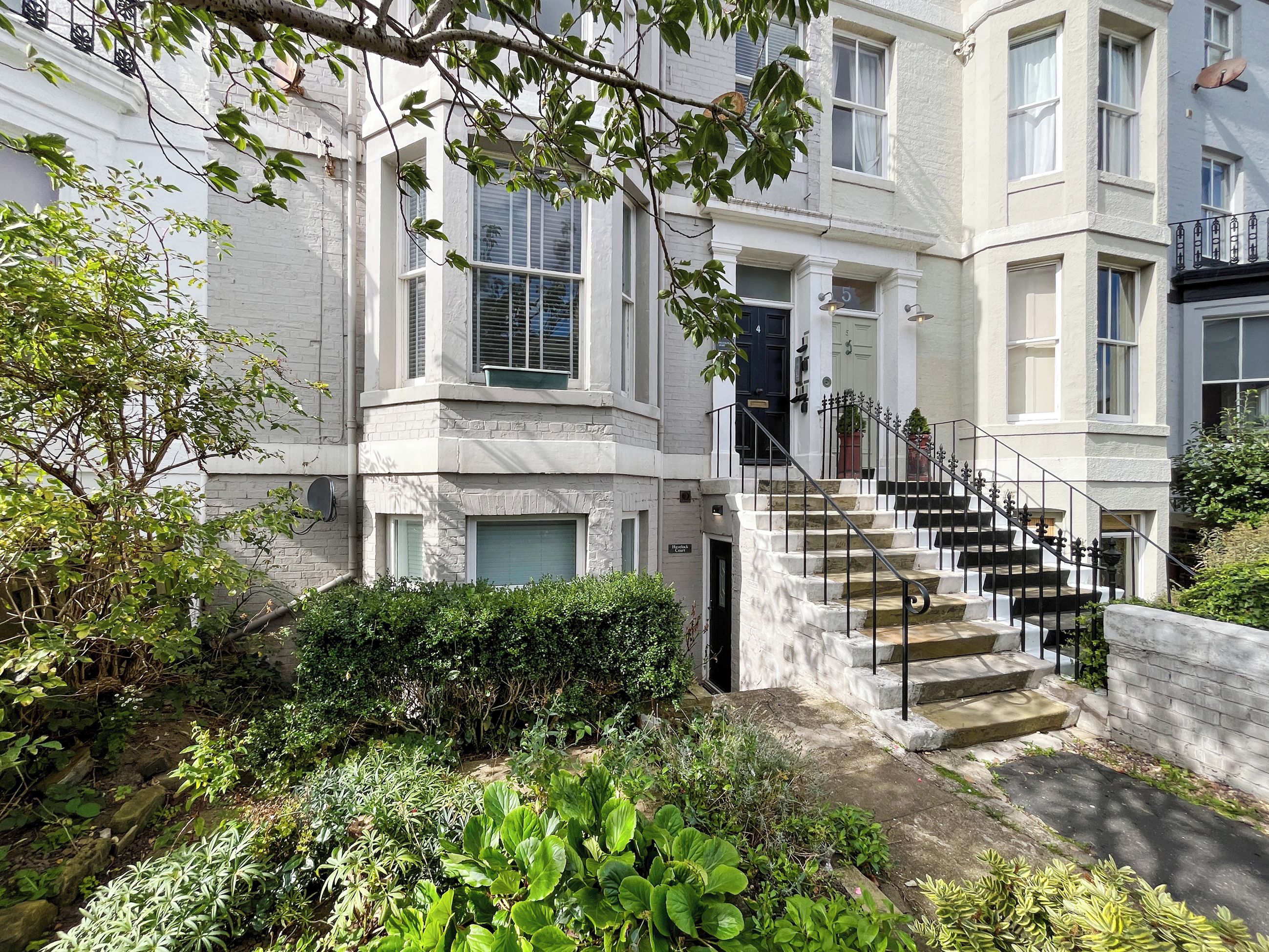 A multi-story residential building with a central staircase, a front door, and a small garden area.