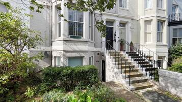 A multi-story residential building with a central staircase, a front door, and a small garden area.