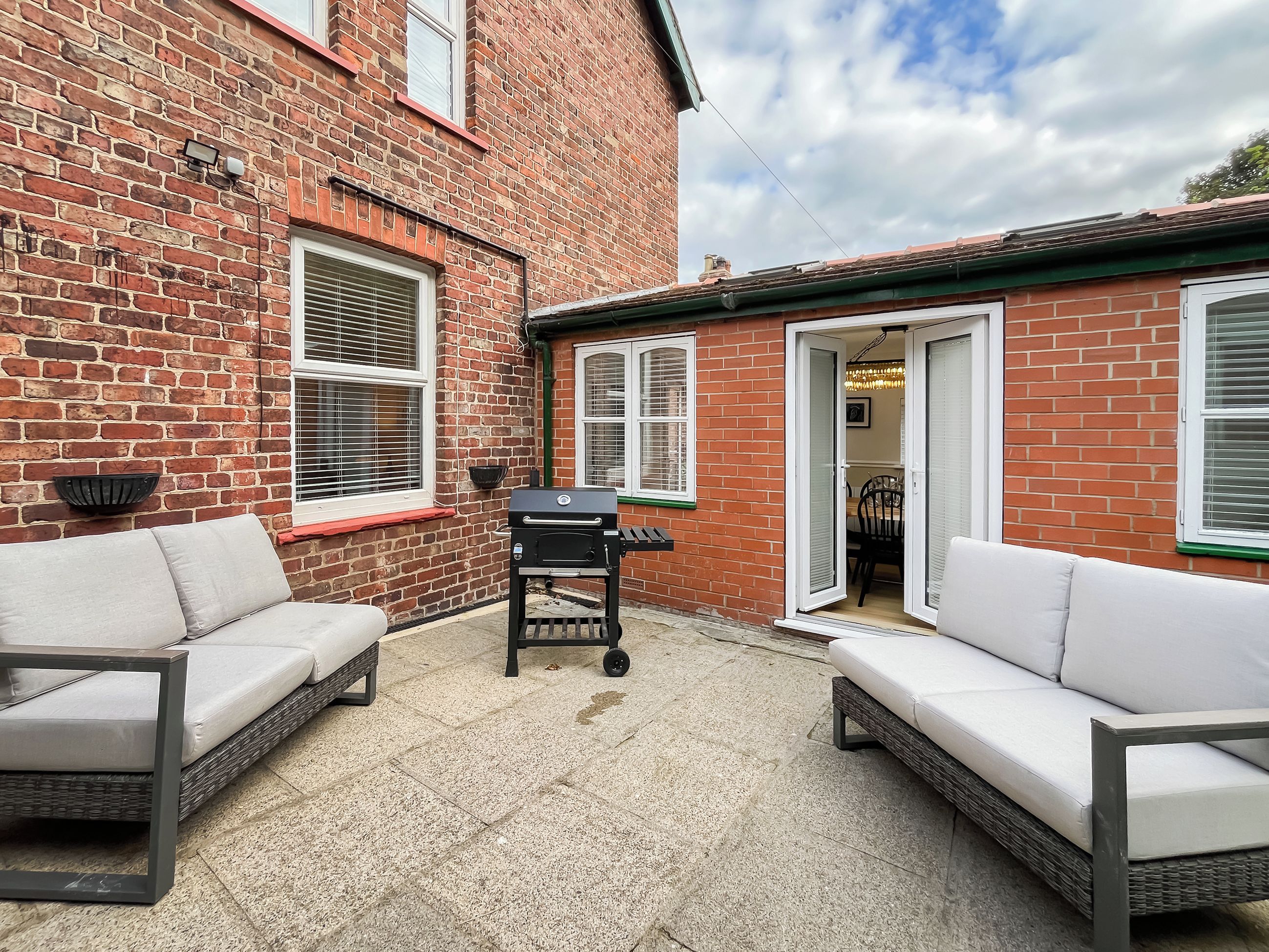 A brick house with a patio area featuring two white sofas and a barbecue grill.
