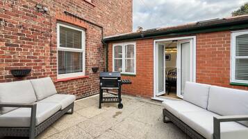 A brick house with a patio area featuring two white sofas and a barbecue grill.
