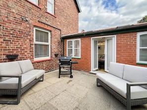 A brick house with a patio area featuring two white sofas and a barbecue grill. - 5 bedroom accommodation in Whitby (Whitby)
