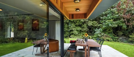 An indoor-outdoor dining area with a glass wall, wooden ceiling, and a garden view.