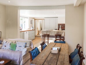 A cozy living area with a sofa, wooden table, and chairs. A kitchen with white cabinets and a dining table is visible in the background. - 3 bedroom accommodation in Rye (Rye)
