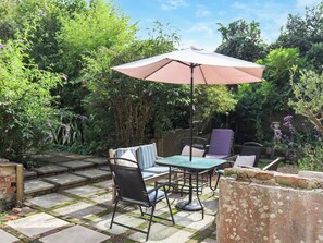 An outdoor patio with a table and chairs, surrounded by lush greenery and a stone pathway. - 3 bedroom accommodation in Rye (Rye)