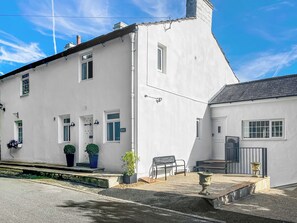 Un bâtiment blanc avec un porche, un banc et un pot de fleurs.