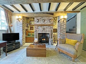 A rustic living room with exposed beams, a fireplace, a sofa, a television, and a bookshelf. - 2 bedroom accommodation in Whitby (Whitby)