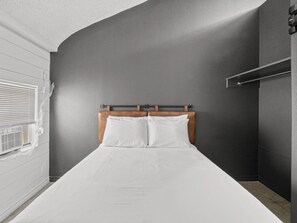 A single bed with a wooden headboard in a room with a dark gray wall and a window with blinds. - Private Coastal Dome with Kitchen - Aransas Pass, TX (Aransas Pass)