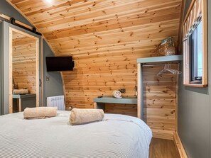 Een slaapkamer met een houten plafond, een bed met twee handdoeken, een aan de muur bevestigde televisie en een kledingkast met een hangroede.