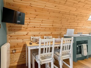Ein gemütliches Blockhaus-Interieur mit Holzbalkendecke, einem Esstisch mit Stühlen, einem an der Wand befestigten Fernseher und einer Küchenzeile.