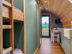 A compact room with bunk beds, a kitchenette, and a view through an open door to the outdoors. - Willow Nook - UK52425 (Blackpool)