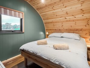 Quarto aconchegante com teto curvo, cama com roupa de cama listrada e janela com vista para árvores.
