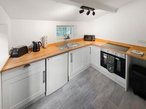 A compact kitchen with white cabinets, a wooden countertop, a built-in dishwasher, and a window with a view of trees. - 1 bedroom accommodation in Oswestry (Oswestry)