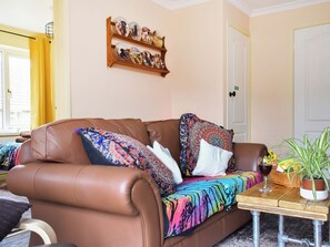 Ein braunes Ledersofa mit bunten Kissen und einer gemusterten Decke, ein Holznachttisch mit einem Glas Wein und eine Wandregal mit Dekorationselementen.