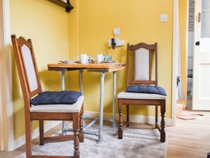 Une pièce comprenant deux chaises en bois avec des assises rembourrées, une petite table avec un plateau et une prise électrique au mur.