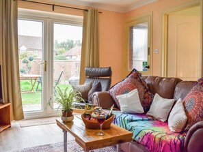 Ein Wohnzimmer mit einer Ledersofa, einem Couchtisch mit Snacks und einem Glas Rotwein, einer Topfpflanze und Blick ins Freie.
