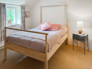 Ein Schlafzimmer mit einem hölzernen Himmelbett, einem Nachttisch mit Lampe und einem Fenster mit Vorhängen.
