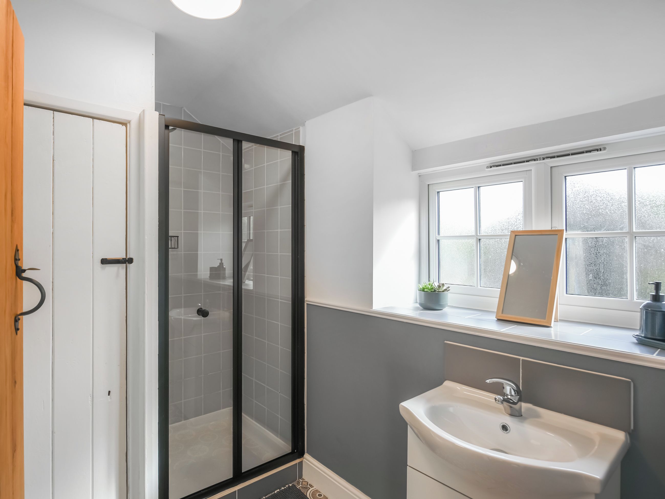 Ein Badezimmer mit Duschkabine aus Glas, Waschbecken, Spiegel und Fenster.