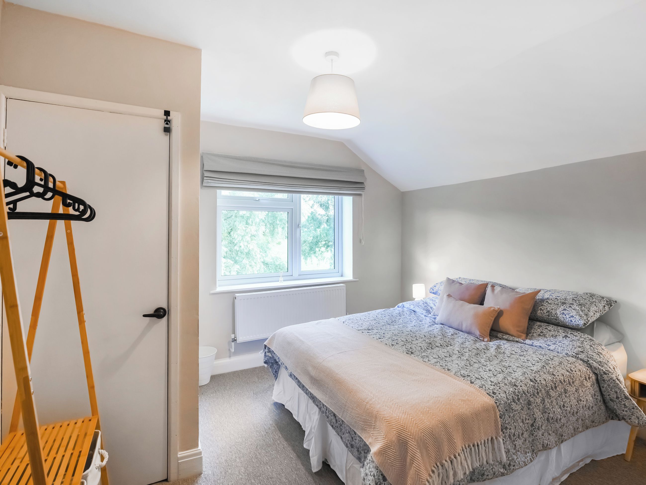 Une chambre à coucher avec un lit, une fenêtre, un luminaire suspendu et une chaise en bois.