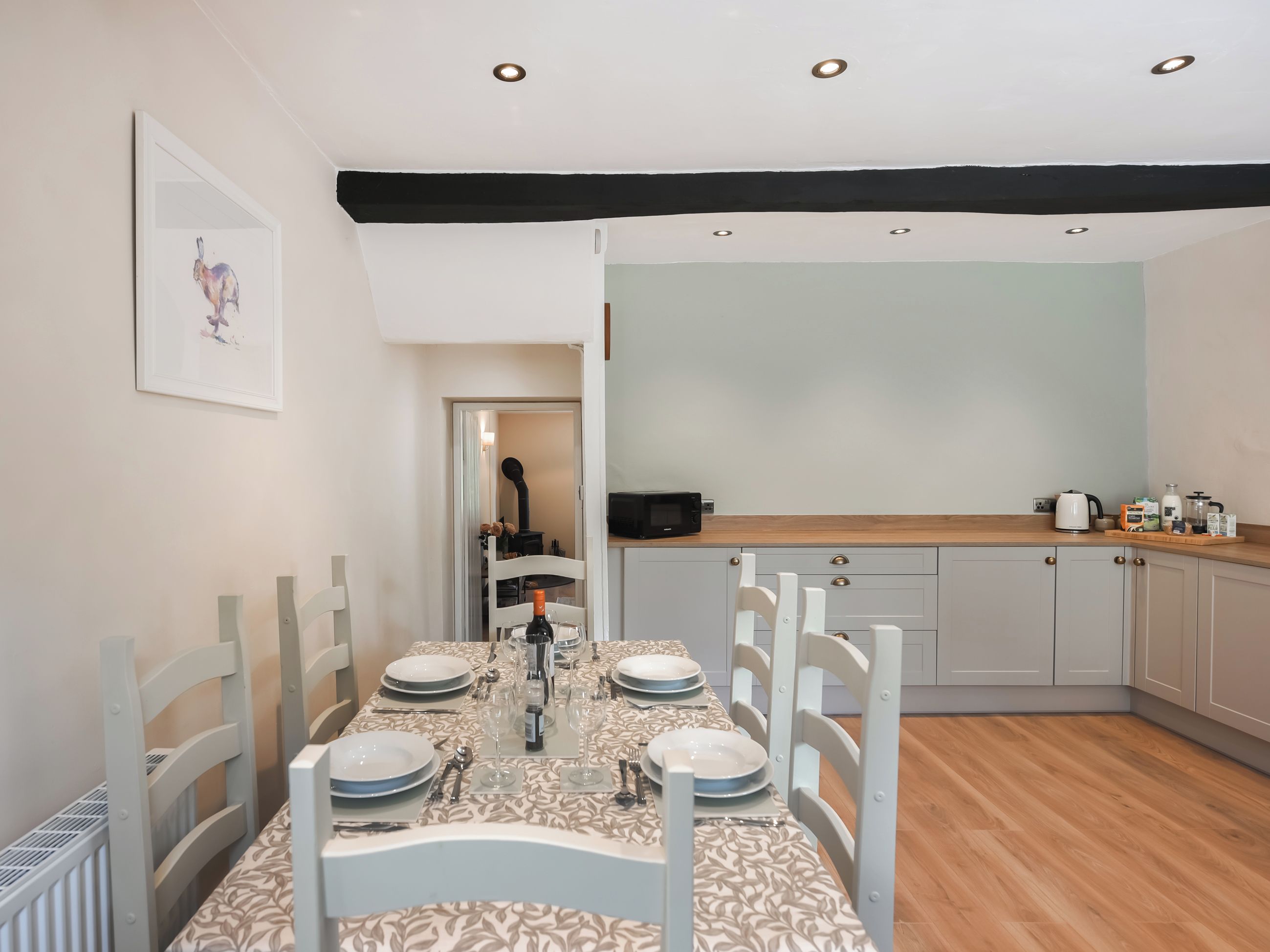 Un comedor con una mesa dispuesta para cuatro, una cocina con electrodomésticos modernos y un acceso a otra habitación.