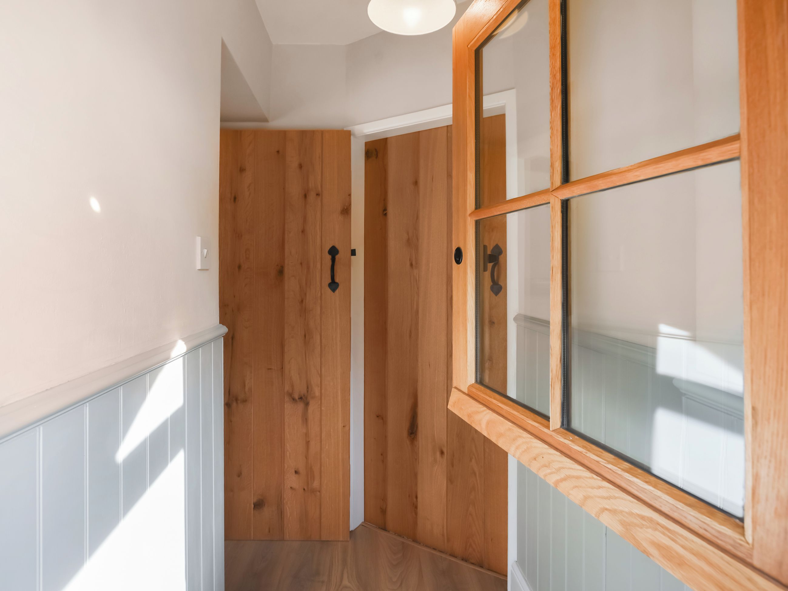 Un pasillo con paneles de madera, una puerta de vidrio con marco de madera y una lámpara de techo blanca.