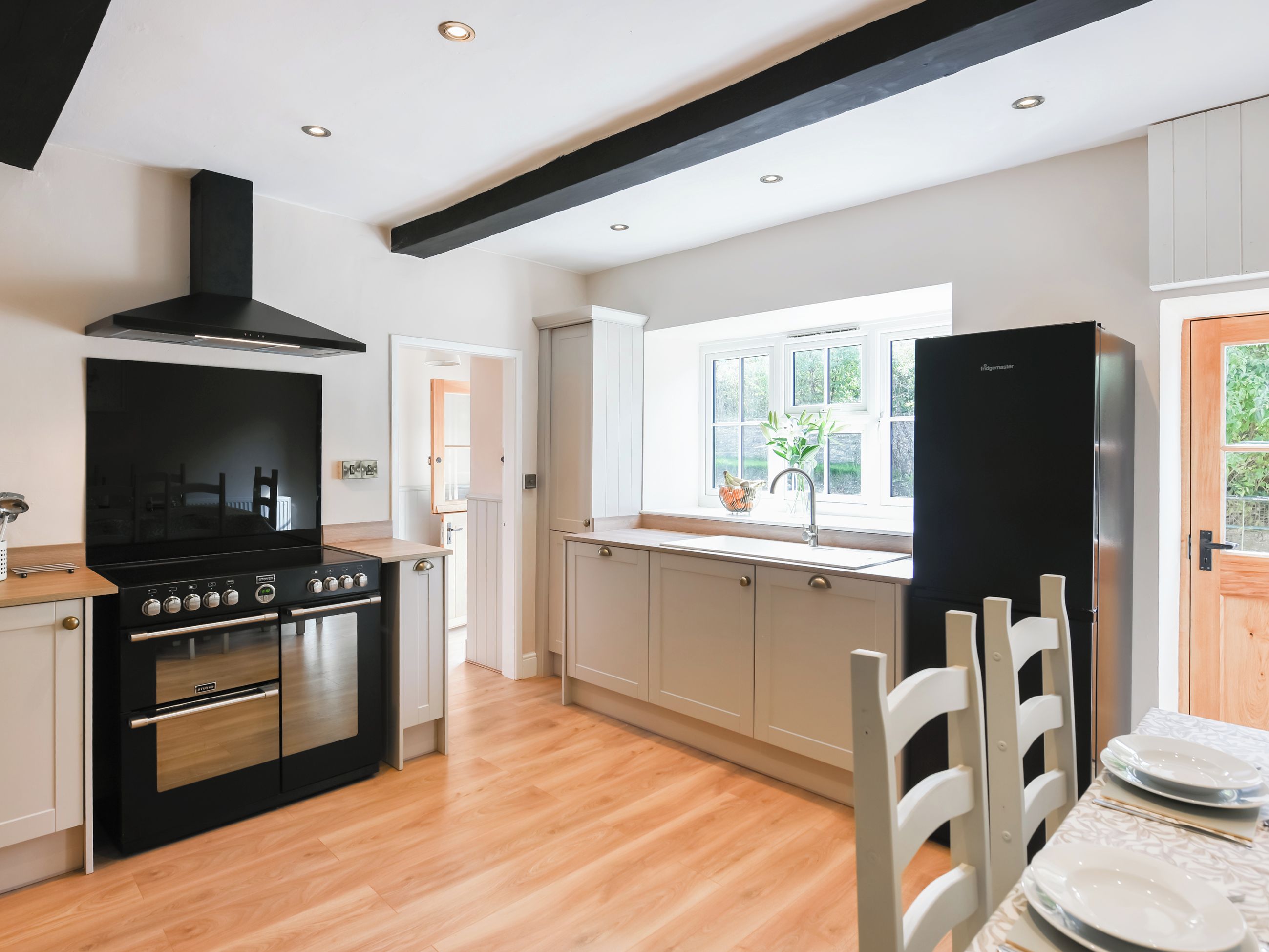 Une cuisine moderne avec un fourneau noir, un four en acier inoxydable et une hotte noire. Une fenêtre offre une vue sur la verdure à l’extérieur.
