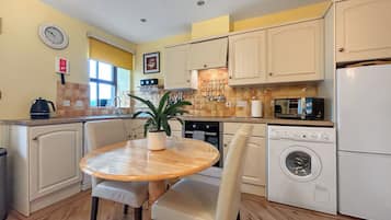 Une cuisine compacte comprenant une table à manger, des chaises, un four à micro-ondes, un lave-linge et une plante en pot.