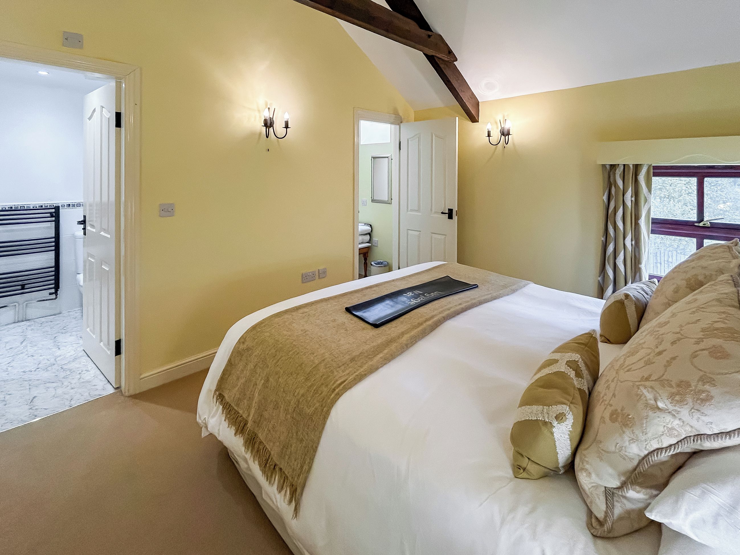 Une chambre à coucher comprenant un lit, une table de chevet, une fenêtre avec des rideaux et une porte donnant sur une salle de bain.