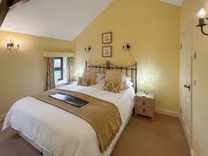 Une chambre à coucher comprenant un lit, des tables de chevet, une fenêtre avec des rideaux et des luminaires fixés au mur.