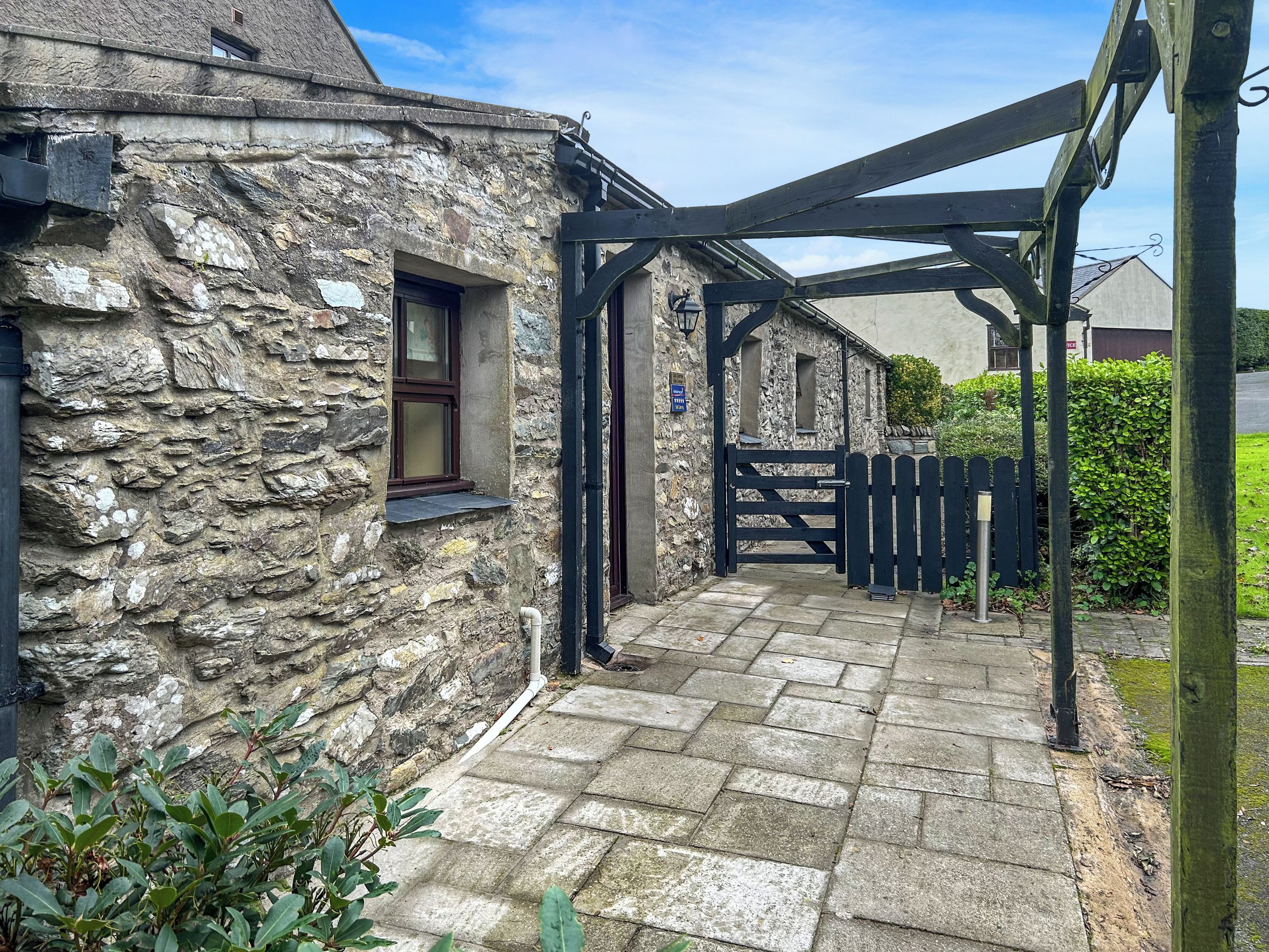 A stone building with a black gate and a wooden pergola.