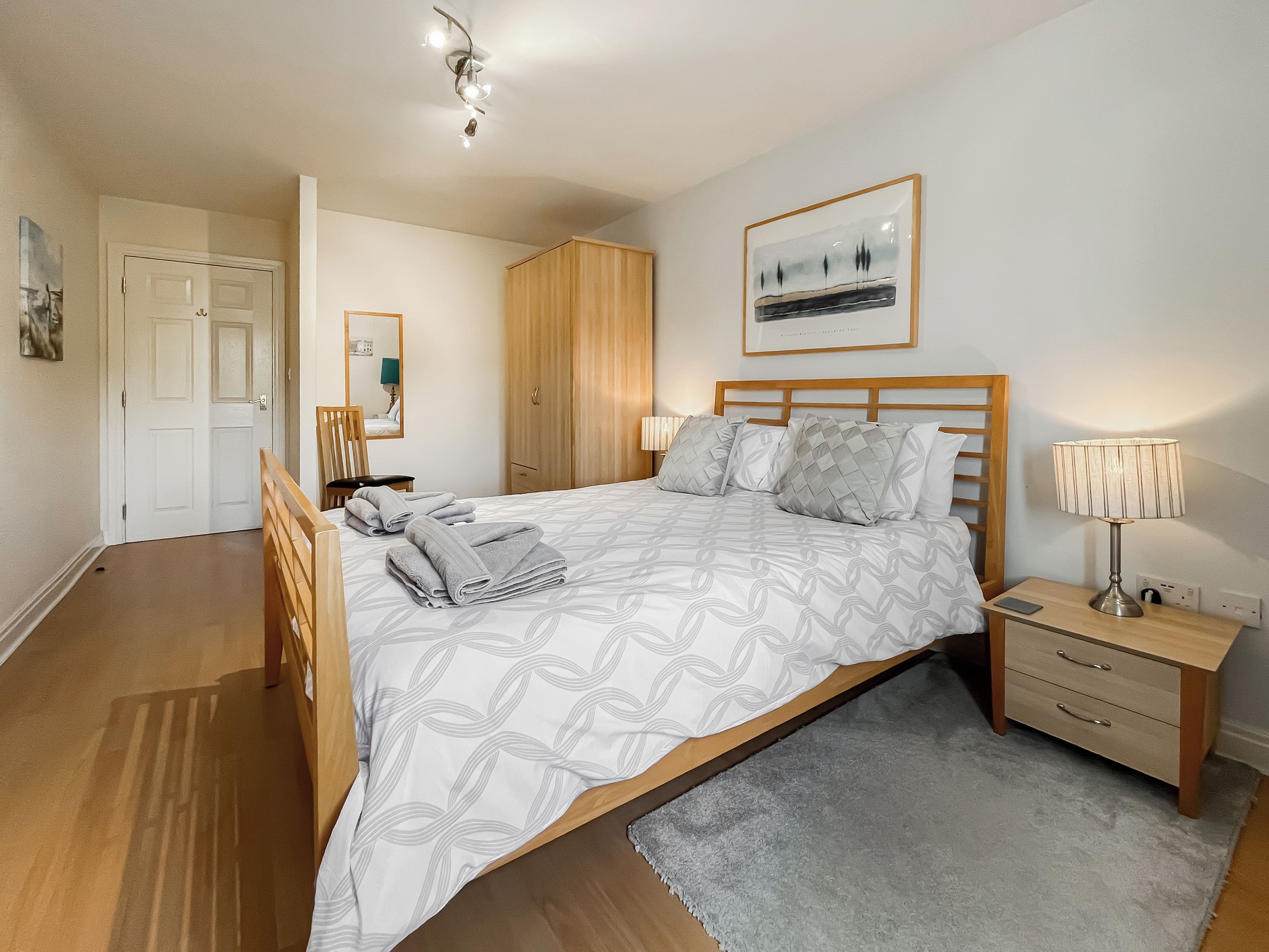A bedroom with a bed, bedside table, lamp, and a framed picture on the wall.