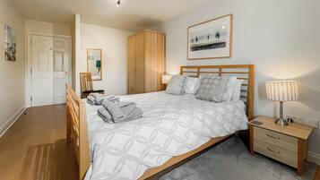 A bedroom with a bed, bedside table, lamp, and a framed picture on the wall.