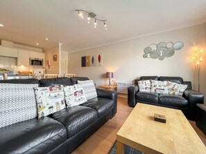 A modern living room with a black leather sofa, a wooden coffee table, and a dining area in the background. - 2 bedroom accommodation in Whitby (Whitby)