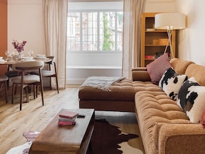 Een gezellige woonkamer met een bank, een salontafel, een eethoek met stoelen en een gedekte tafel, en een raam met uitzicht op gebouwen.