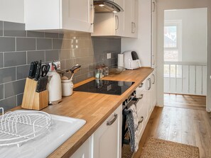 Cocina moderna con tope de inducción negro, armarios blancos y encimera de madera.