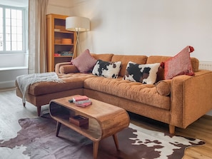 A cozy living room with a sectional sofa, a wooden coffee table, a cowhide rug, and a bookshelf with board games. - 2 bedroom accommodation in Minehead (Minehead)