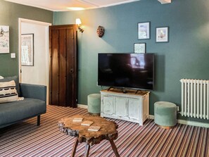 A living room with a television, a sofa, a coffee table, and a patterned carpet. - Old Post Office Cottage (Weymouth)