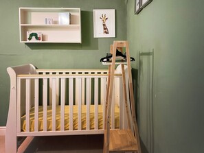 A crib with a wooden ladder, a white shelf with books, and a framed picture on the wall. - Old Post Office Cottage (Weymouth)