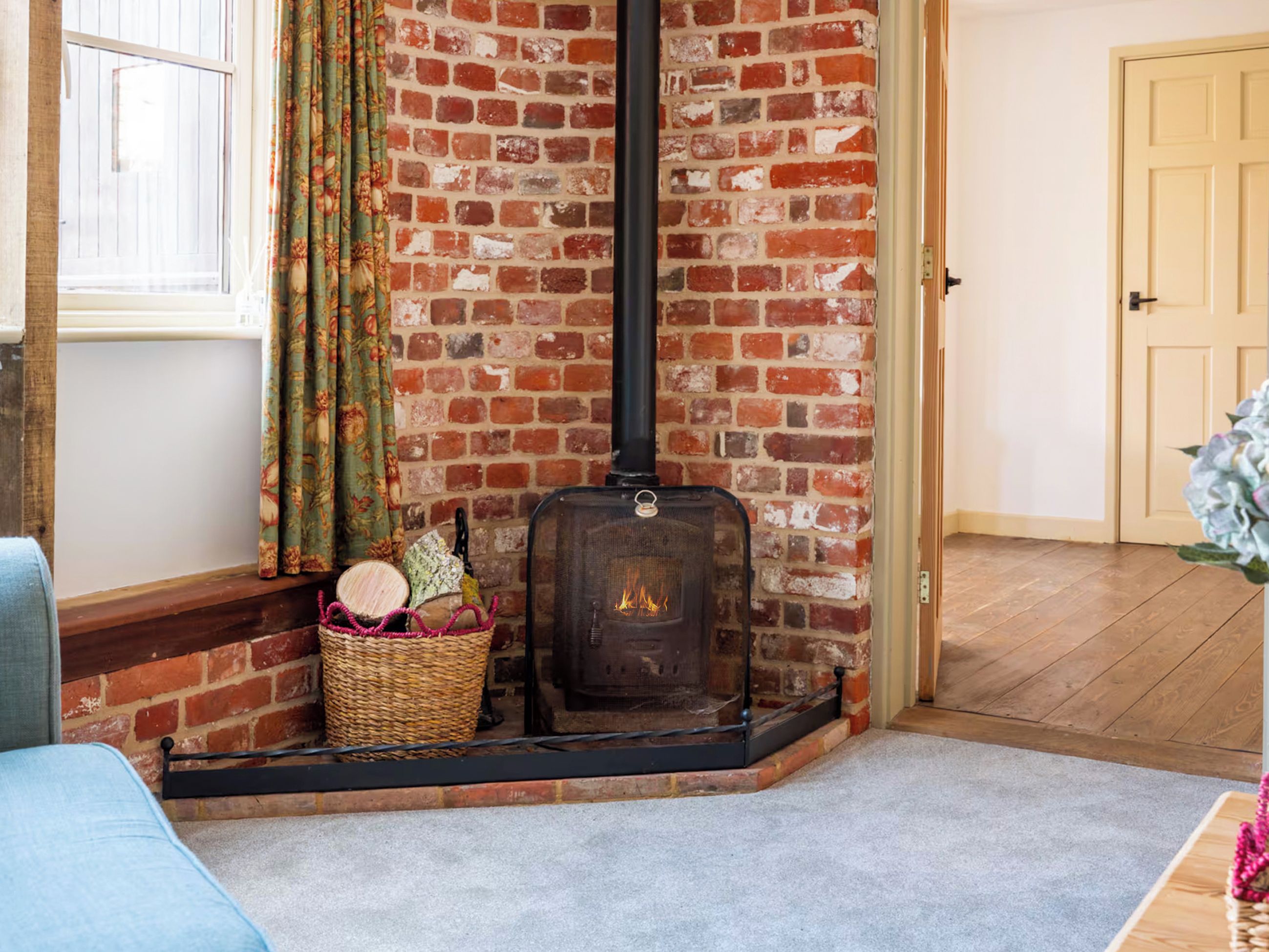 A room with a brick wall, a fireplace, a window with curtains, and a door.