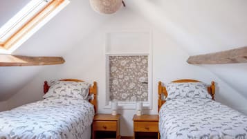 A bedroom with two beds, wooden headboards, a window with floral wallpaper, and a hanging light fixture.